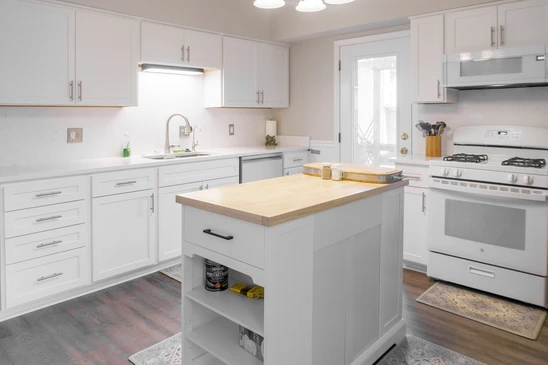 Une cuisine moderne et lumineuse avec des armoires blanches, des appareils en acier inoxydable et un îlot central avec un comptoir en bois, créant un espace propre et fonctionnel