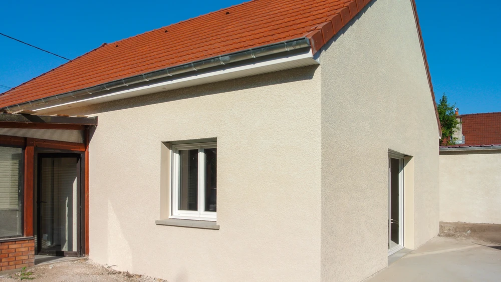 Extension de maison plain-pied, façade enduit gratté beige clair, toiture en tuiles canal terre cuite rouge avec gouttière zinc