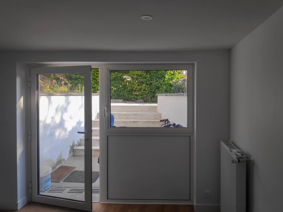 Intérieur d'une pièce rénovée avec une porte-fenêtre double vantail PVC blanc ouverte sur un jardin avec escalier en béton