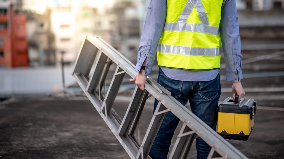 Homme d'affaires mature en costume sombre et casque de sécurité blanc sur chantier de construction, bras croisés, expression confiante
