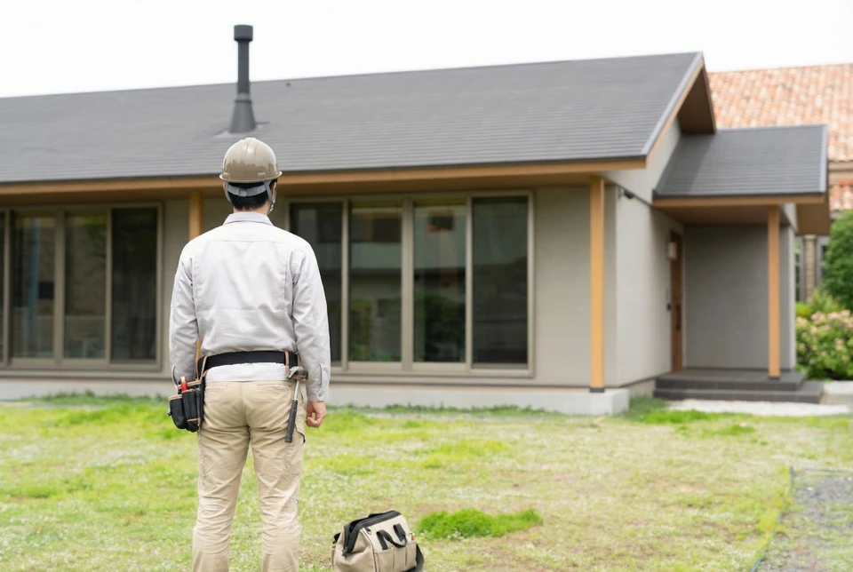 Professionnel en uniforme bleu devant pavillon résidentiel, tenant clipboard et stylo